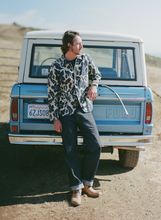 Man leaning against a vintage Ford truck in a desert setting